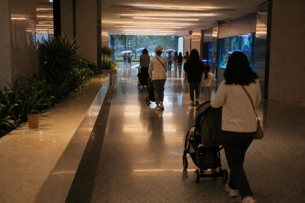 Families with strollers moving through a bright aquarium corridor between tanks, no text, no logos, no people
