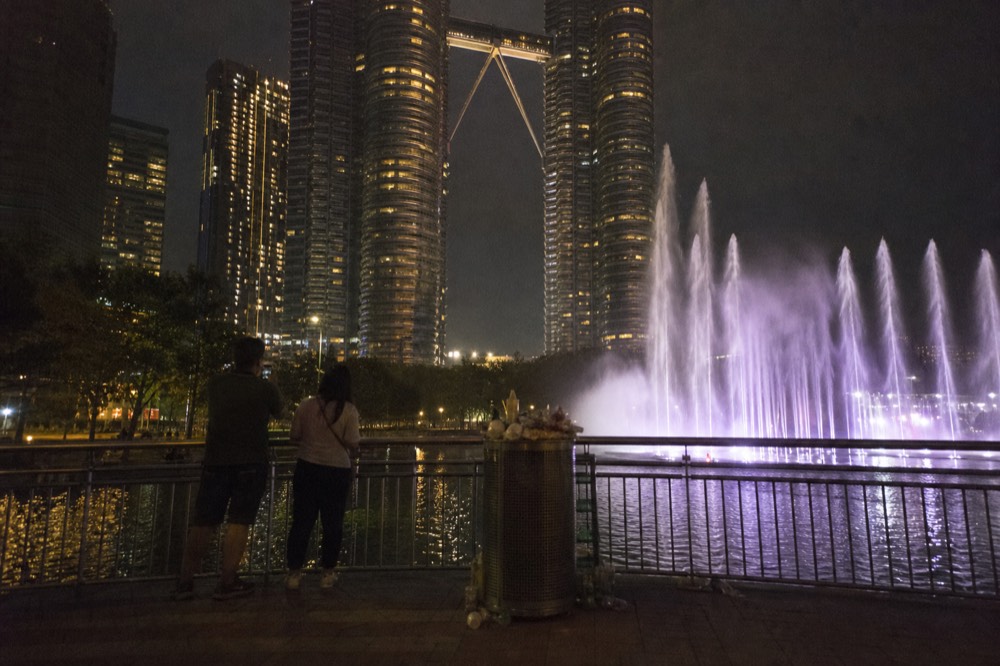 KLCC Park fountain show at night with Petronas Towers lit up, no text, no logos, no people