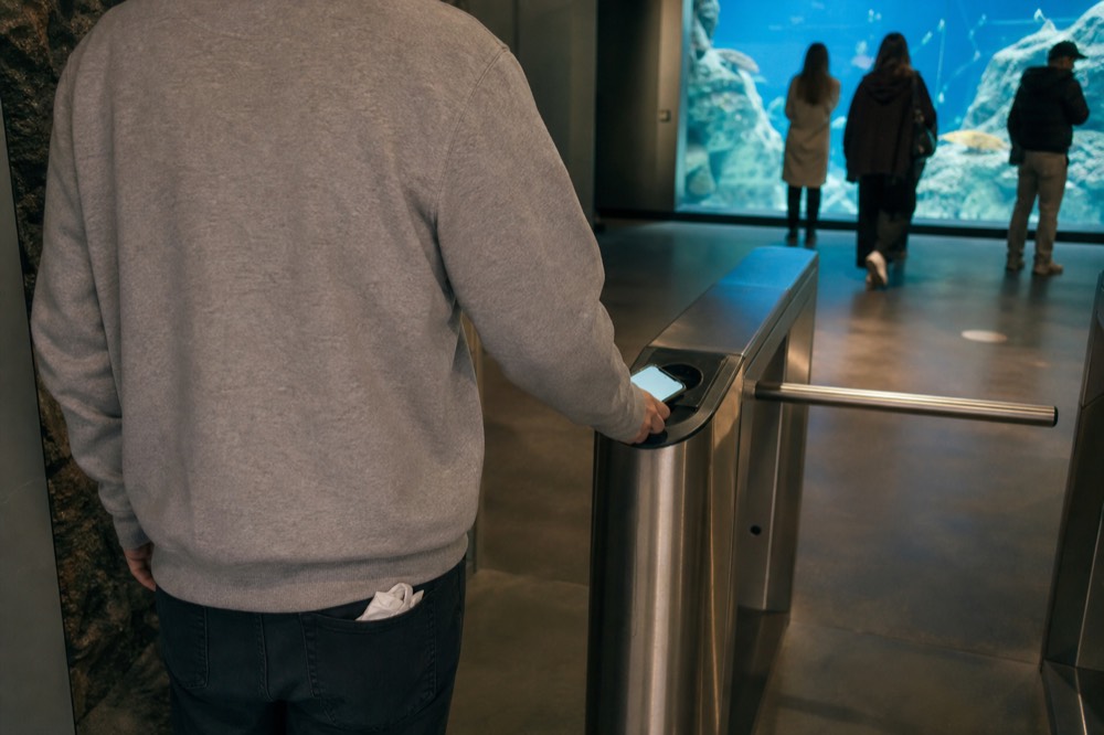 Visitor scanning a phone e-ticket at an aquarium turnstile, no text, no logos, no people