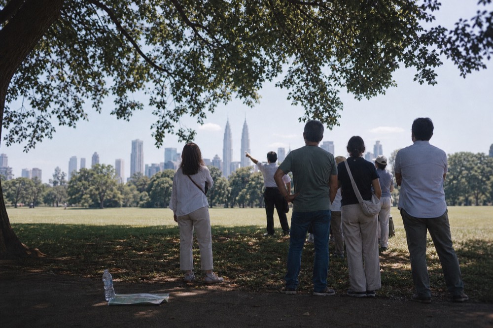 A guide pointing toward the Petronas Twin Towers while a small group gathers in KLCC Park, no text, no logos, no people