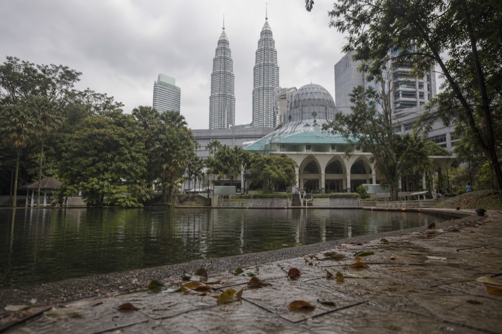 The domed KLCC Mosque framed by trees with the towers rising behind, no text, no logos, no people