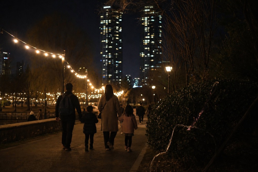 A family walking a lit park path toward the illuminated towers at night, no text, no logos, no people