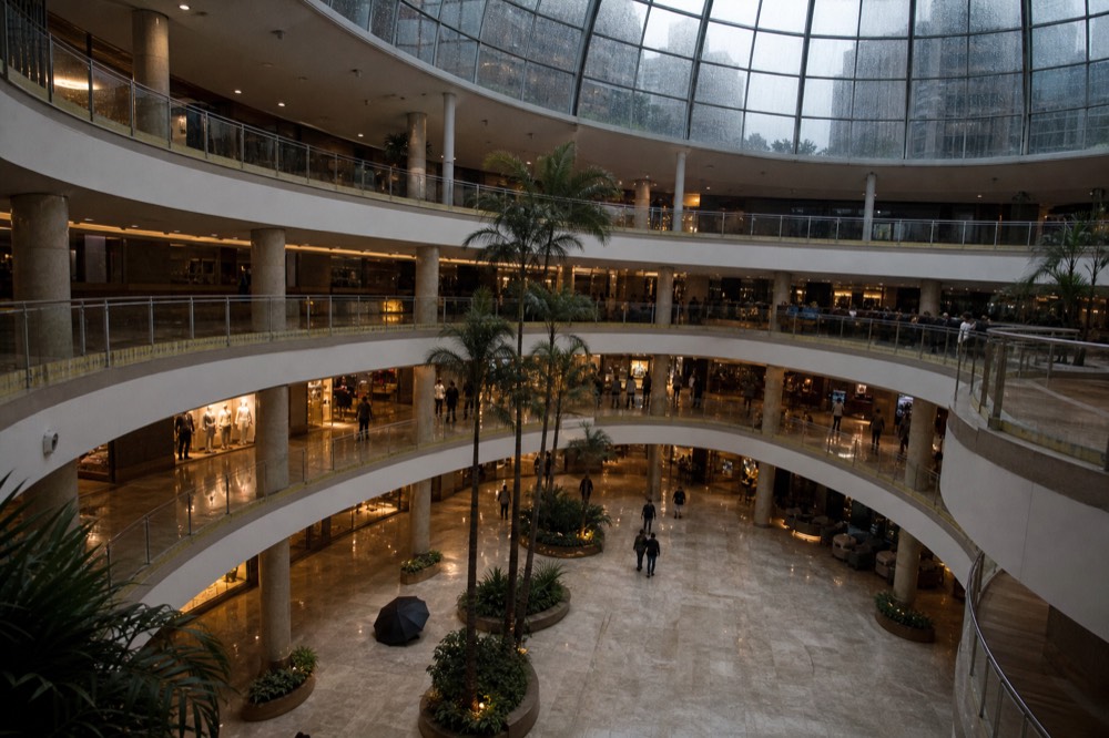 Tall glass atrium with palm trees inside a shopping centre, no text, no logos, no people