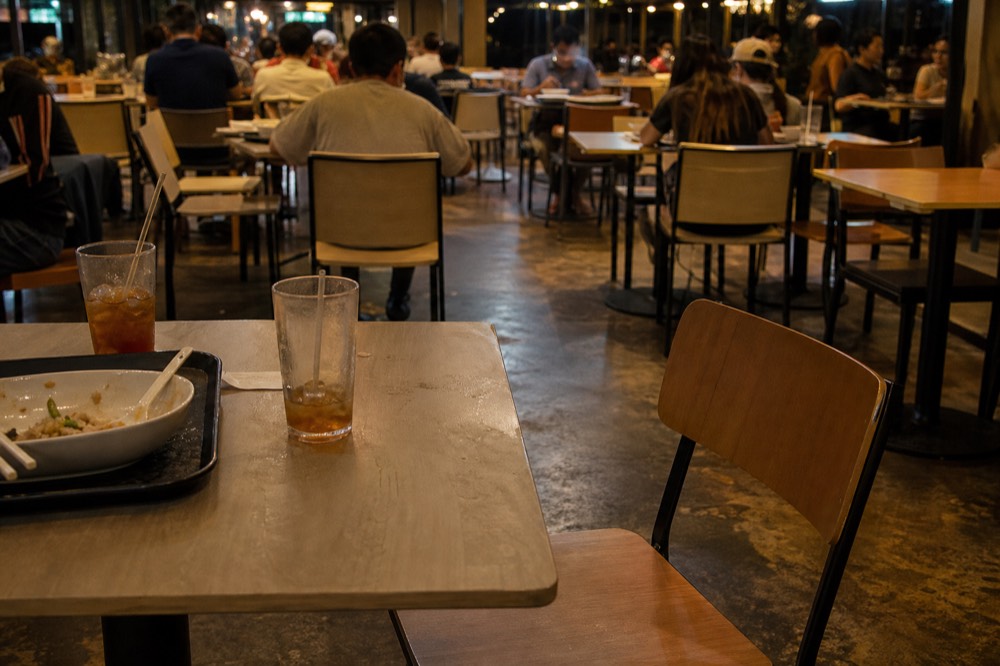 Food court tables under warm lighting with trays of food, no text, no logos, no people